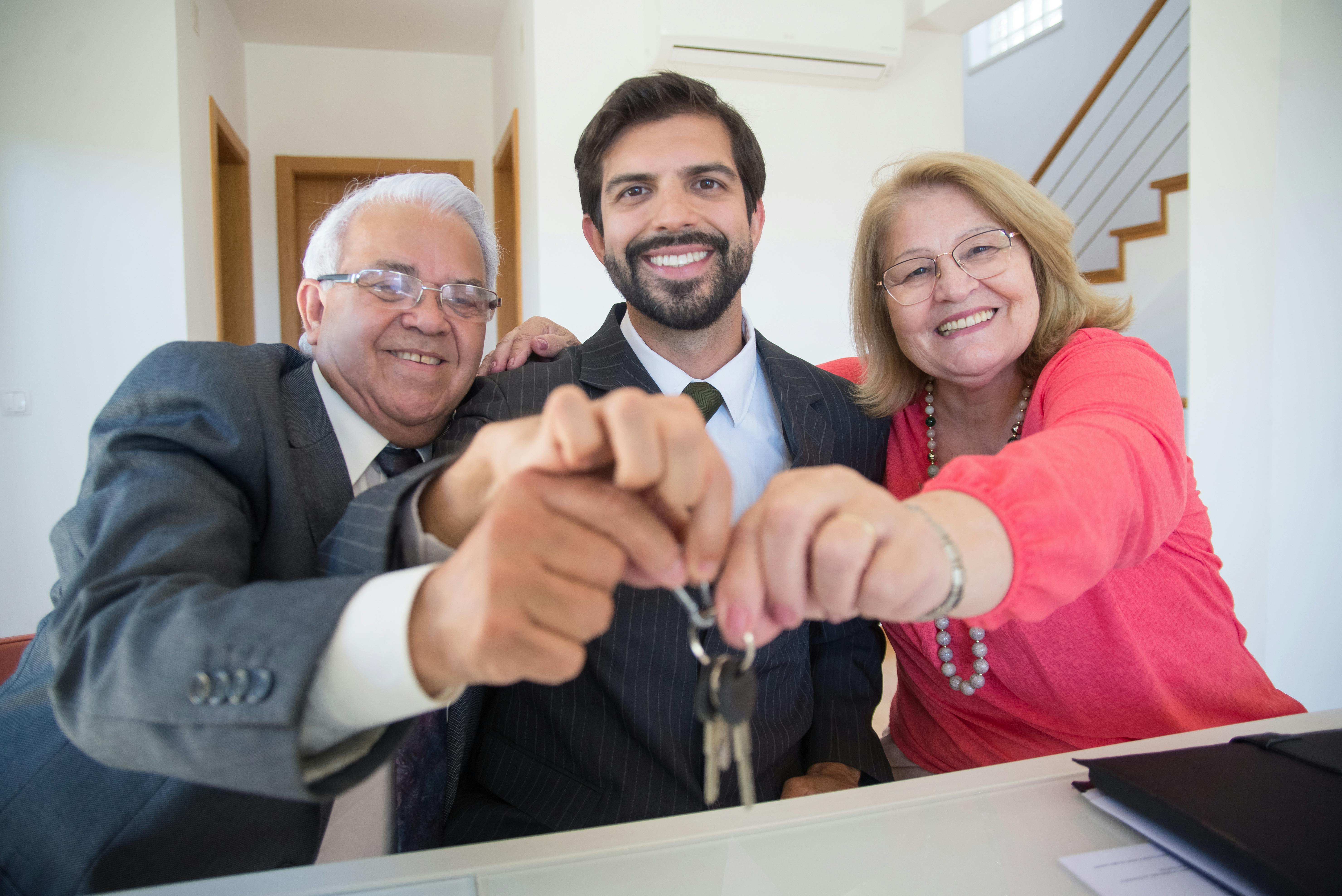Elderly%20Couple%20Holding%20Keys%20of%20a%20House%20Beside%20a%20Person%20in%20Black%20Suit%20Jacket